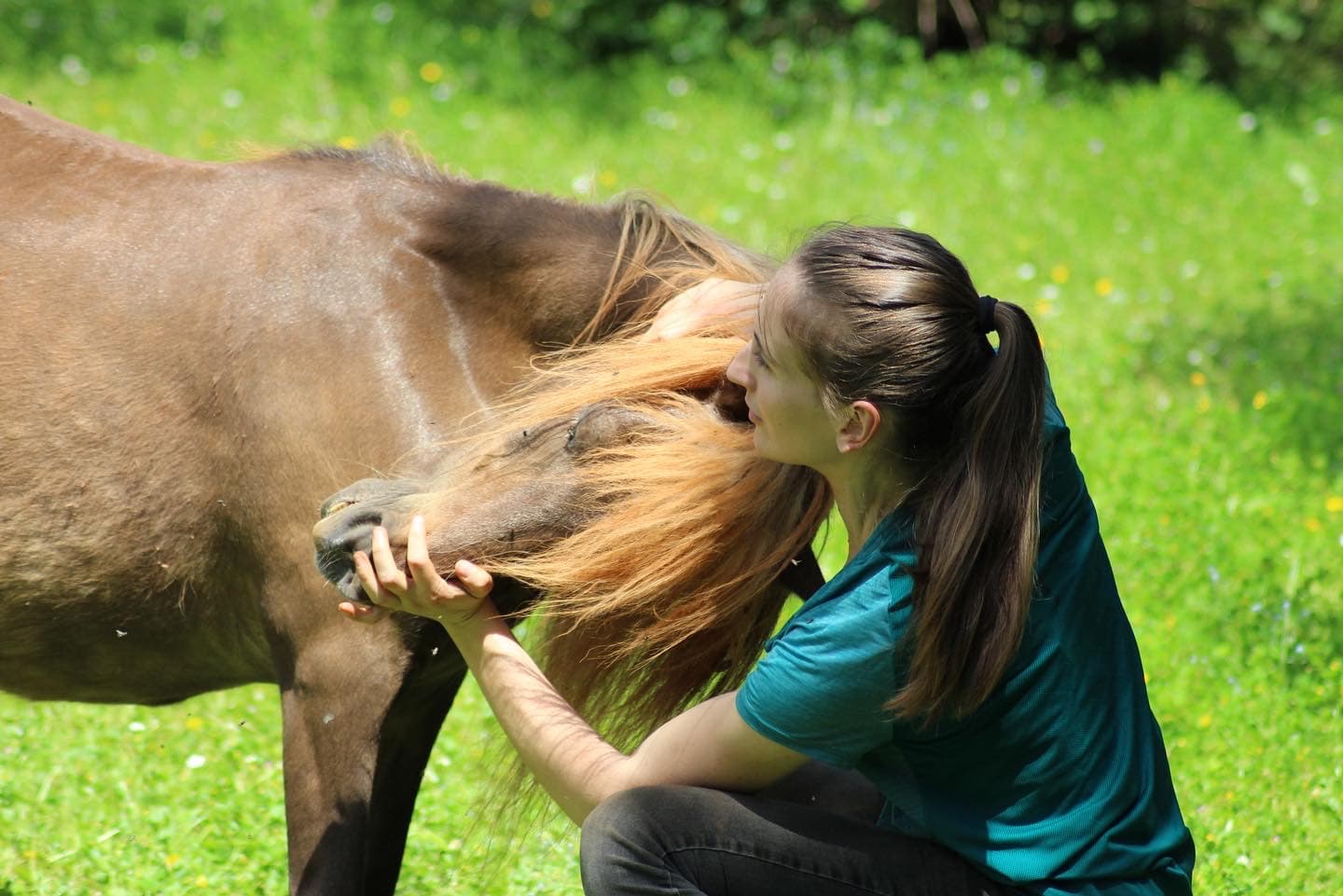 Marie Salabert soutient l'encolure d'un poney brun dans un pré fleuri.