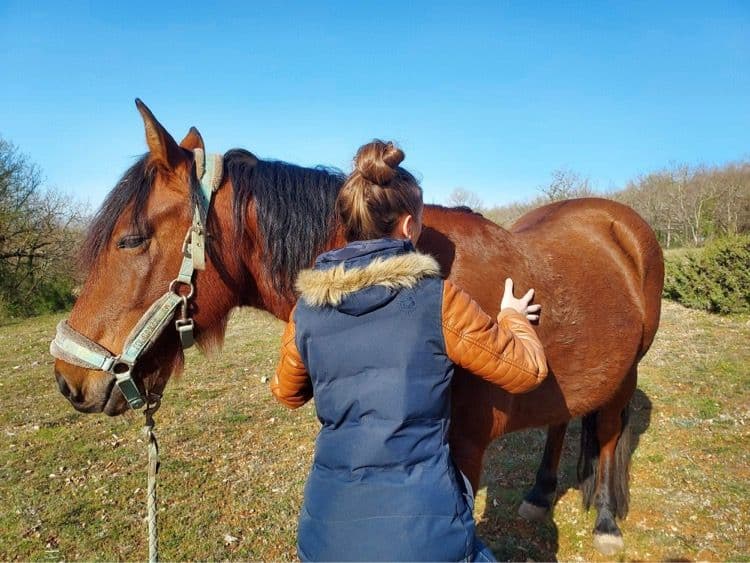 Marie Salabert pose les mains sur le flanc d'un cheval bai au pré