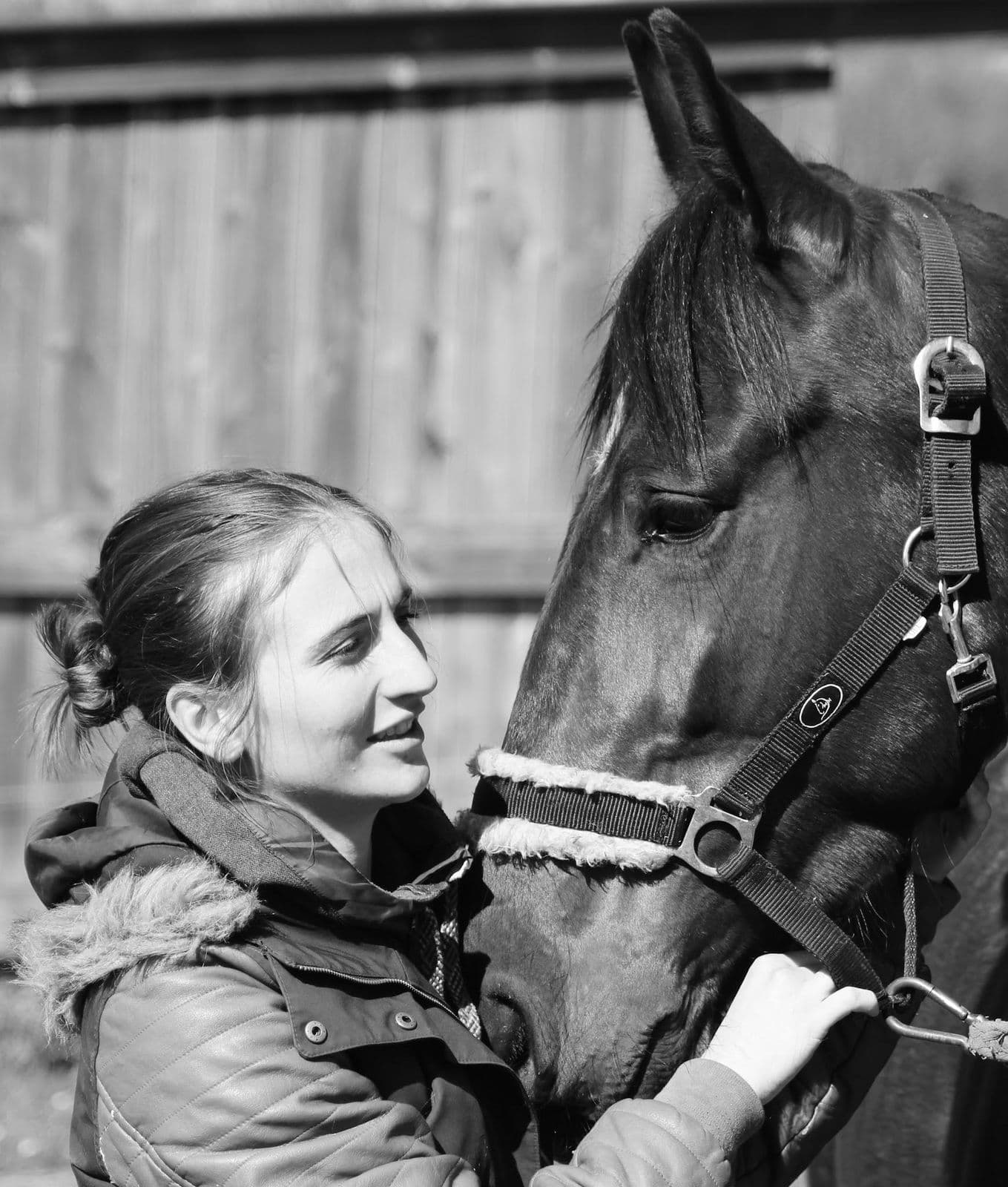 Marie Salabert souriante, joue contre la tête d'un cheval bai